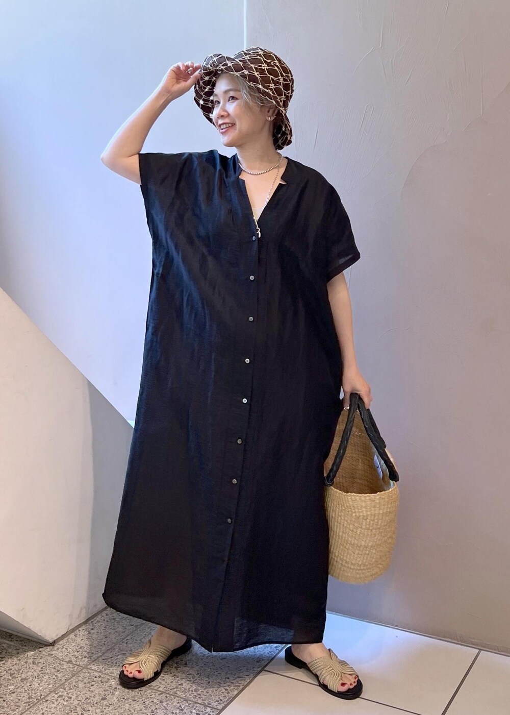 ゴールド系のサンダル、ブラック系のワンピース、ベージュ系のかごバッグを着用したレディースの夏コーディネートの2枚目の写真