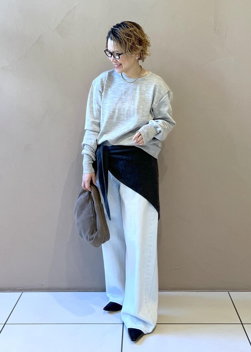 ブルー系のデニムパンツ、グレー系のハンドバッグ、ブラック系のパンプスを着用したレディースの秋コーディネートの2枚目の写真