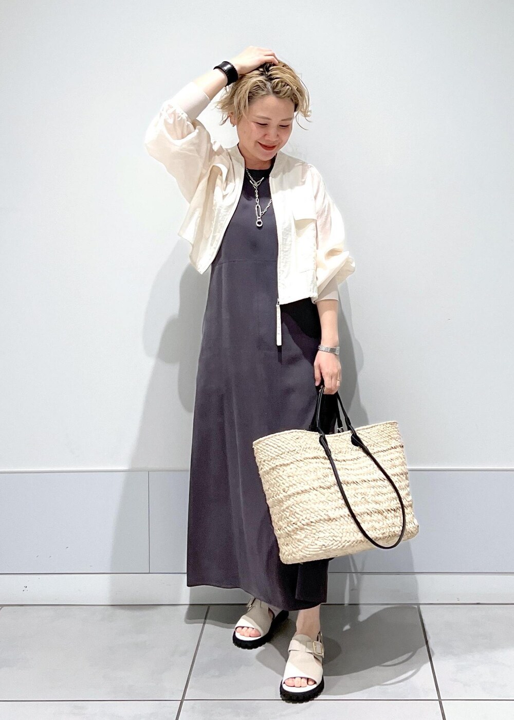 ホワイト系のサンダル、ホワイト系のブルゾン、グレー系のワンピースを着用したレディースの春コーディネートの2枚目の写真