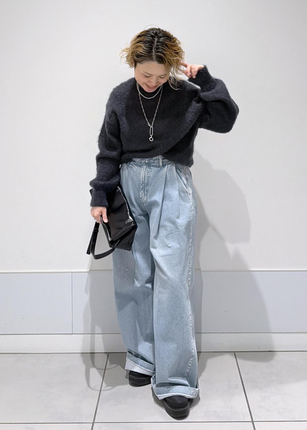 ブラック系のショルダーバッグ、ブラック系のブーツ、ブルー系のデニムパンツを着用したレディースの秋コーディネートの3枚目の写真