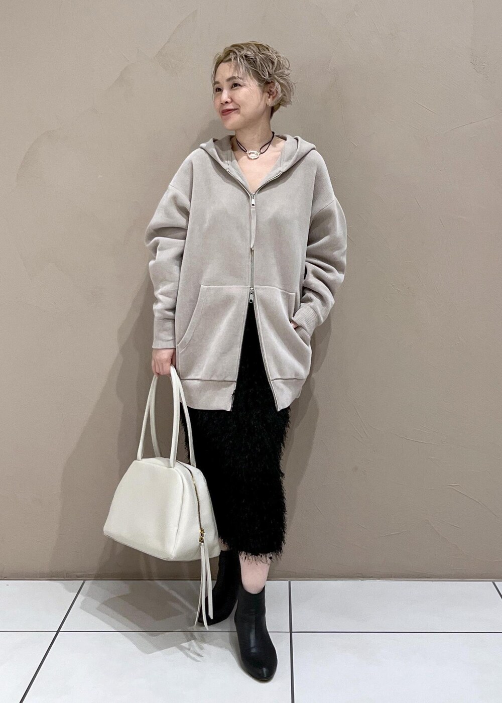 ベージュ系のパーカー、ホワイト系のボストンバッグ、ブラック系のブーツを着用したレディースの秋コーディネートの4枚目の写真