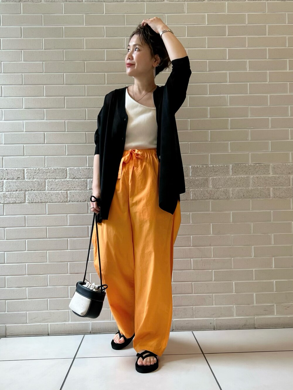 ブラック系のカーディガン/ボレロ、オレンジ系のパンツ、ブラック系のショルダーバッグを着用したレディースの夏コーディネートの3枚目の写真