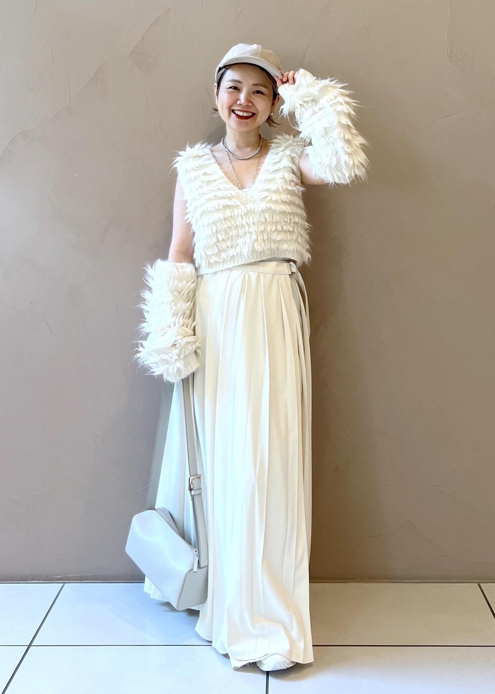 グレー系のショルダーバッグ、ホワイト系のベスト、ホワイト系のキャップを着用したレディースの秋コーディネートの3枚目の写真