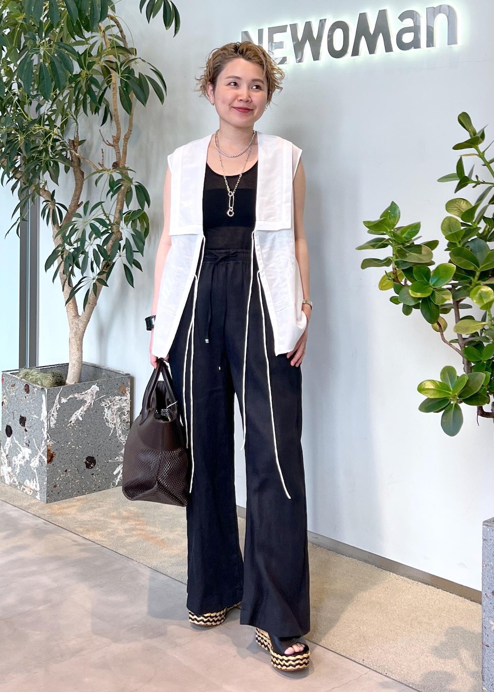 ブラック系のその他パンツ、ブラウン系のトートバッグ、ホワイト系のシャツ/ブラウスを着用したレディースの夏コーディネートの2枚目の写真