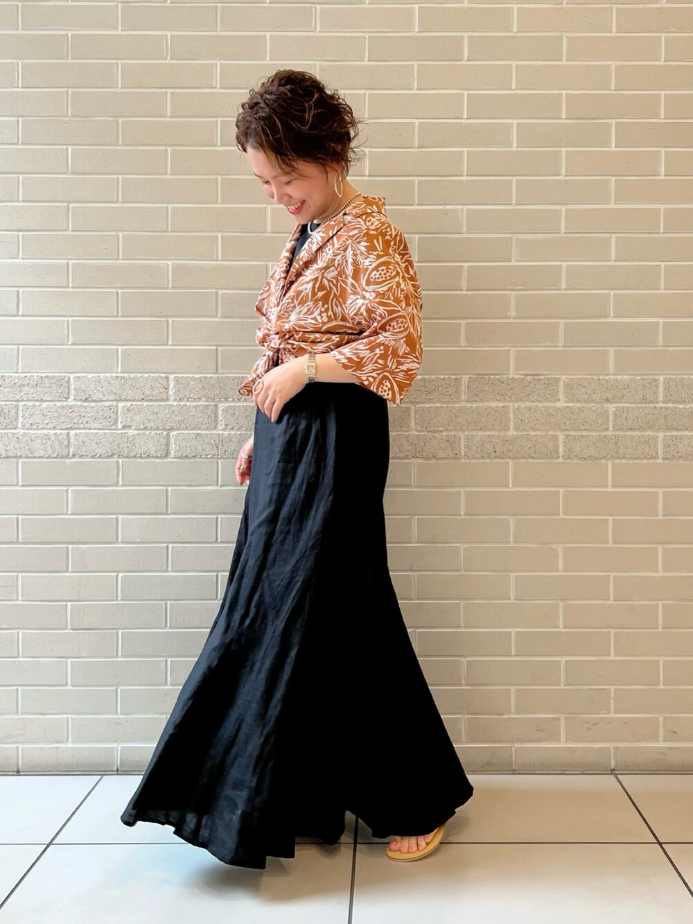 オレンジ系のシャツ/ブラウス、ブラック系のワンピース、シルバー系のサンダルを着用したレディースの夏コーディネートの2枚目の写真