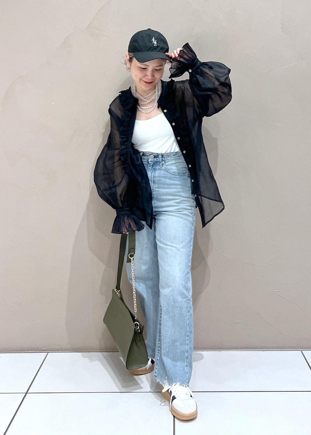 グリーン系のショルダーバッグ、ブルー系のデニムパンツ、ホワイト系のスニーカーを着用したレディースの夏コーディネートの3枚目の写真