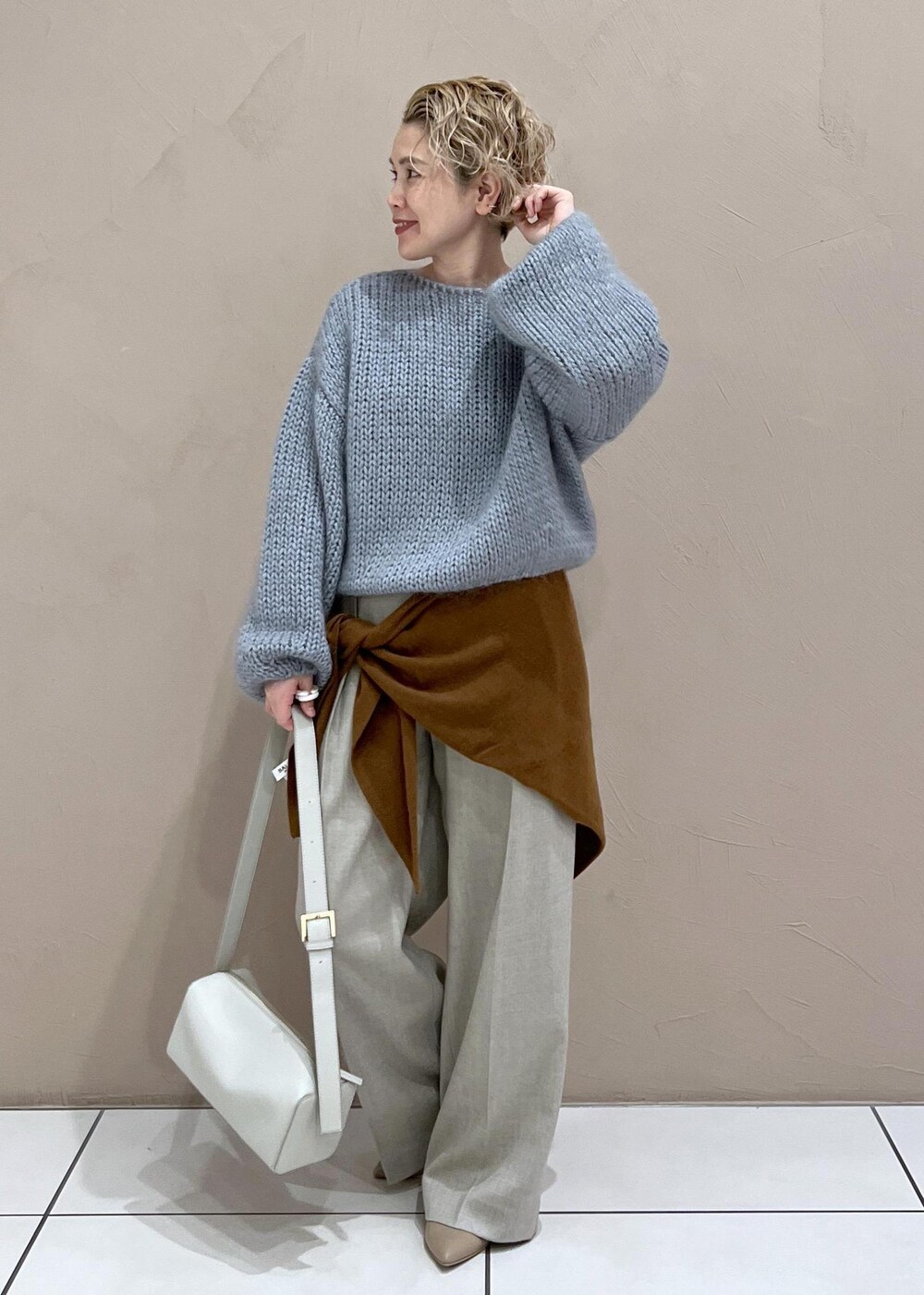 グレー系のショルダーバッグ、ベージュ系のスラックス、ブルー系のニット/セーターを着用したレディースの秋コーディネートの3枚目の写真
