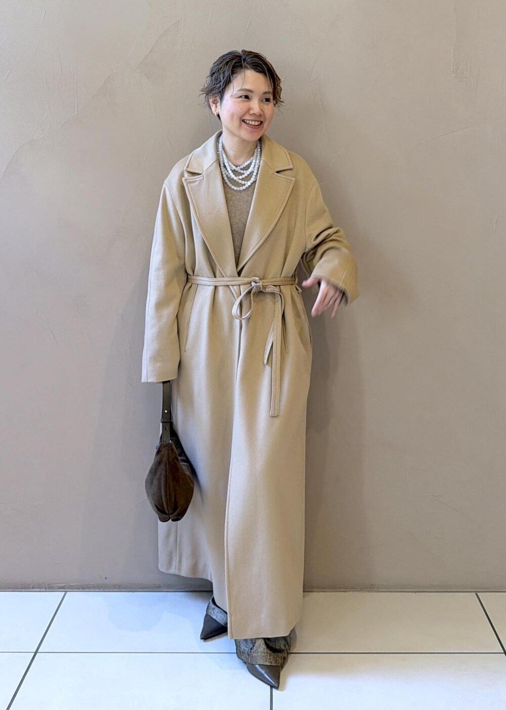 イエロー系のトレンチコート、ゴールド系のその他パンツ、ベージュ系のニット/セーターを着用したレディースの冬コーディネートの2枚目の写真