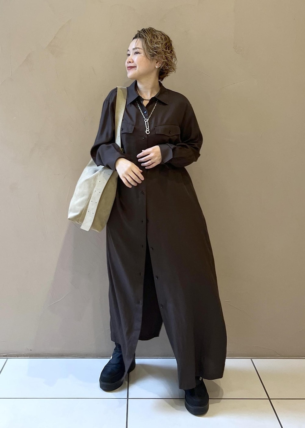 ベージュ系のショルダーバッグ、グレー系のワンピース、ブラック系のブーツを着用したレディースの秋コーディネートの4枚目の写真