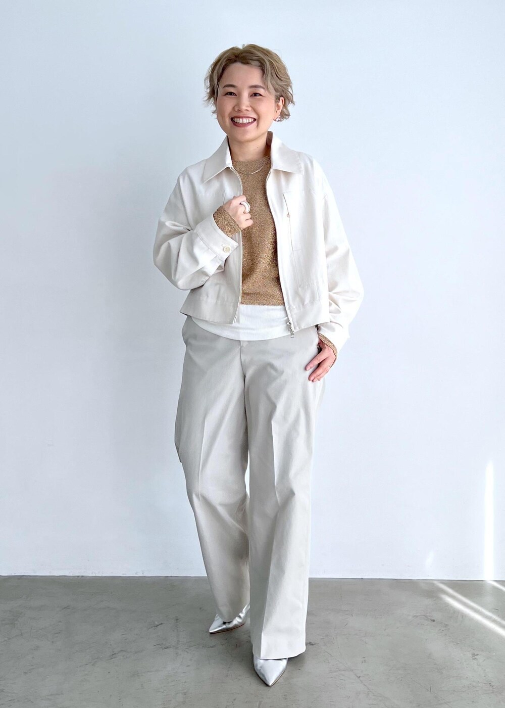 ホワイト系のブルゾン、ゴールド系のTシャツ/カットソー、グレー系のスラックスを着用したレディースの春コーディネートの3枚目の写真