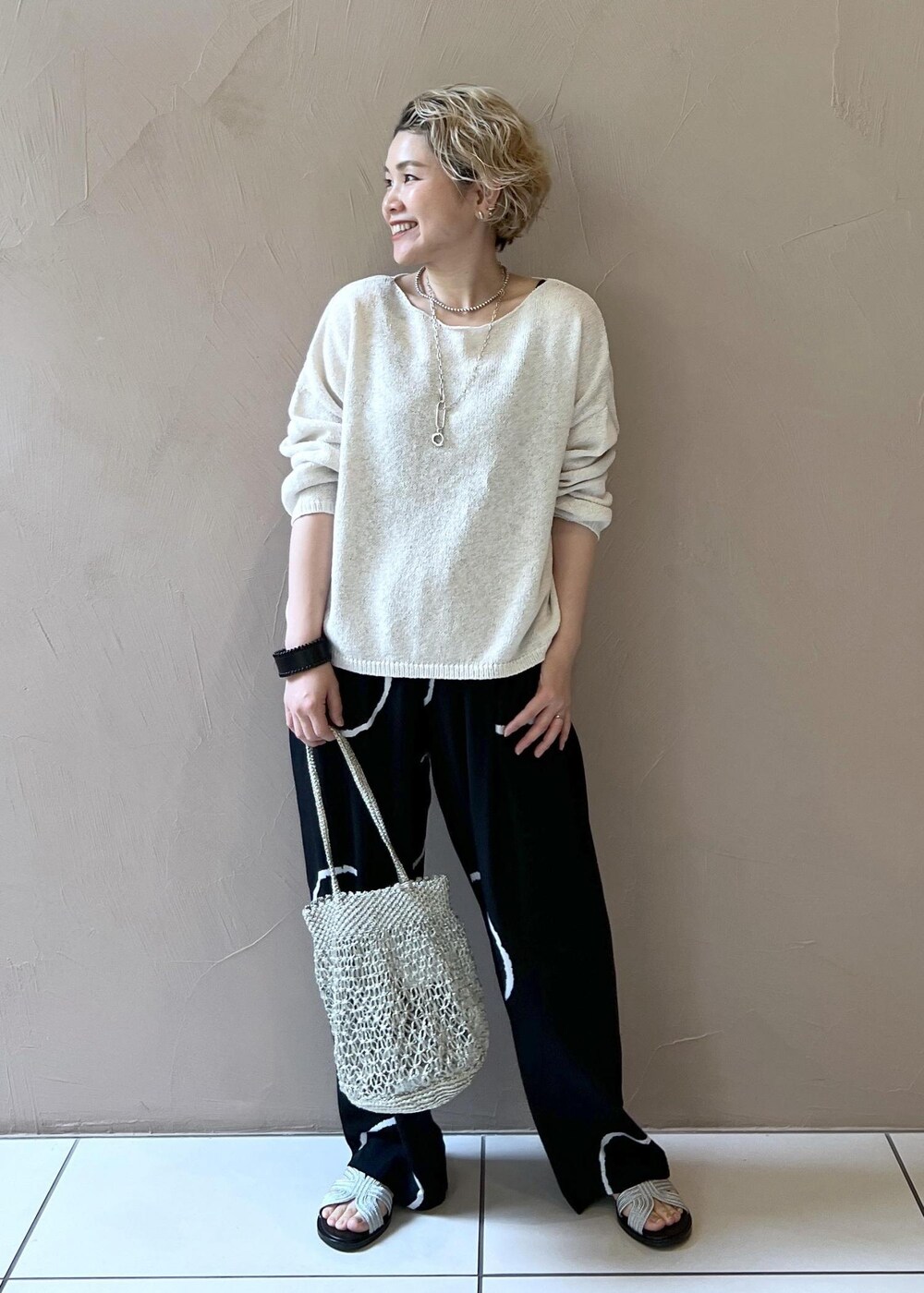 ゴールド系のハンドバッグ、シルバー系のサンダル、ホワイト系のニット/セーターを着用したレディースの春コーディネートの3枚目の写真