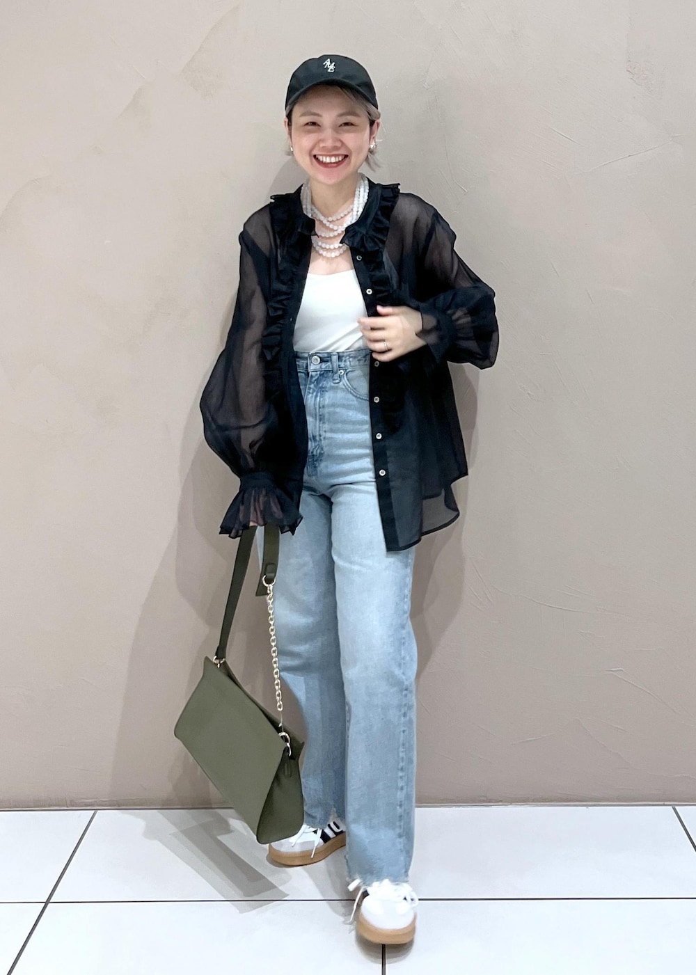 グリーン系のショルダーバッグ、ブルー系のデニムパンツ、ホワイト系のスニーカーを着用したレディースの夏コーディネートの2枚目の写真