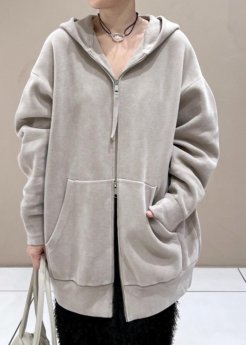 ベージュ系のパーカー、ホワイト系のボストンバッグ、ブラック系のブーツを着用したレディースの秋コーディネートの6枚目の写真