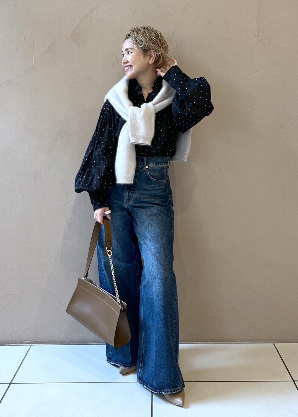 グレー系のニット/セーター、ブルー系のデニムパンツ、ブラウン系のショルダーバッグを着用したレディースの秋コーディネートの2枚目の写真
