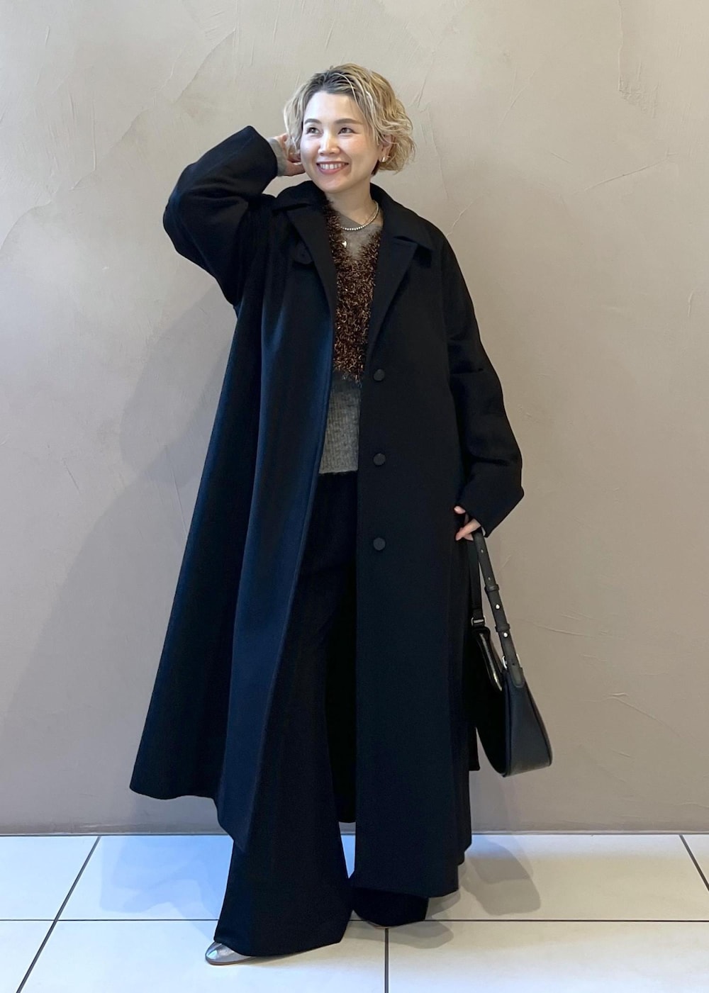 ブラック系のベスト、グレー系のニット/セーター、ブラック系のステンカラーコートを着用したレディースの冬コーディネートの2枚目の写真