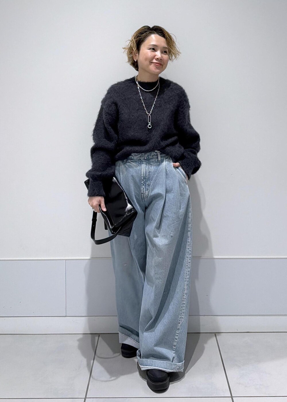 ブラック系のショルダーバッグ、ブラック系のブーツ、ブルー系のデニムパンツを着用したレディースの秋コーディネートの2枚目の写真