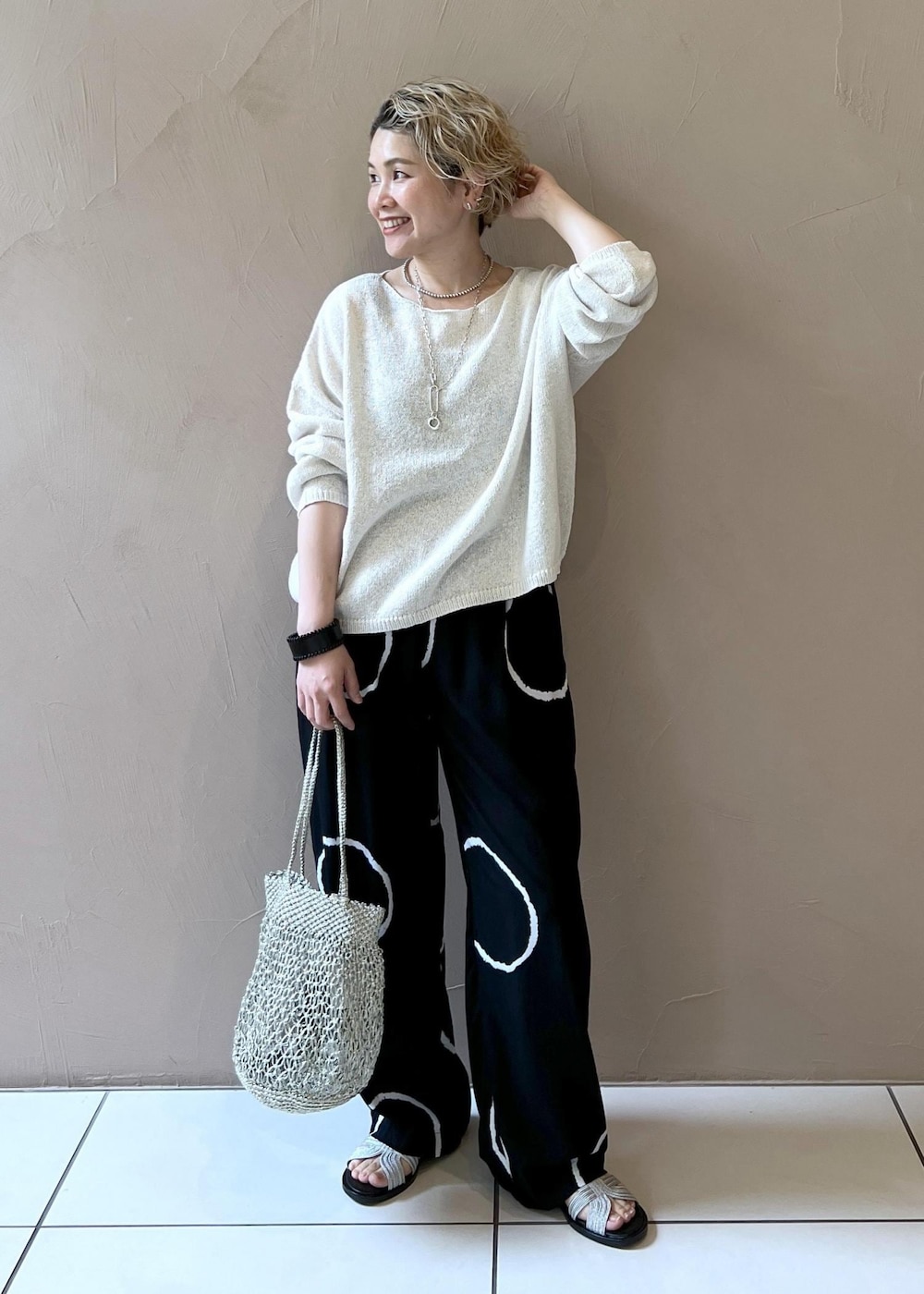 ゴールド系のハンドバッグ、シルバー系のサンダル、ホワイト系のニット/セーターを着用したレディースの春コーディネートの2枚目の写真