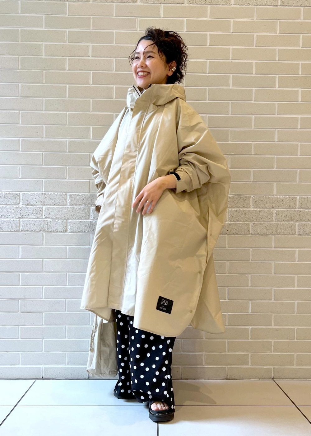 ベージュ系のトートバッグ、ブラック系のつなぎ/オールインワン、ベージュ系のレインコート/ポンチョを着用したレディースの夏コーディネートの3枚目の写真