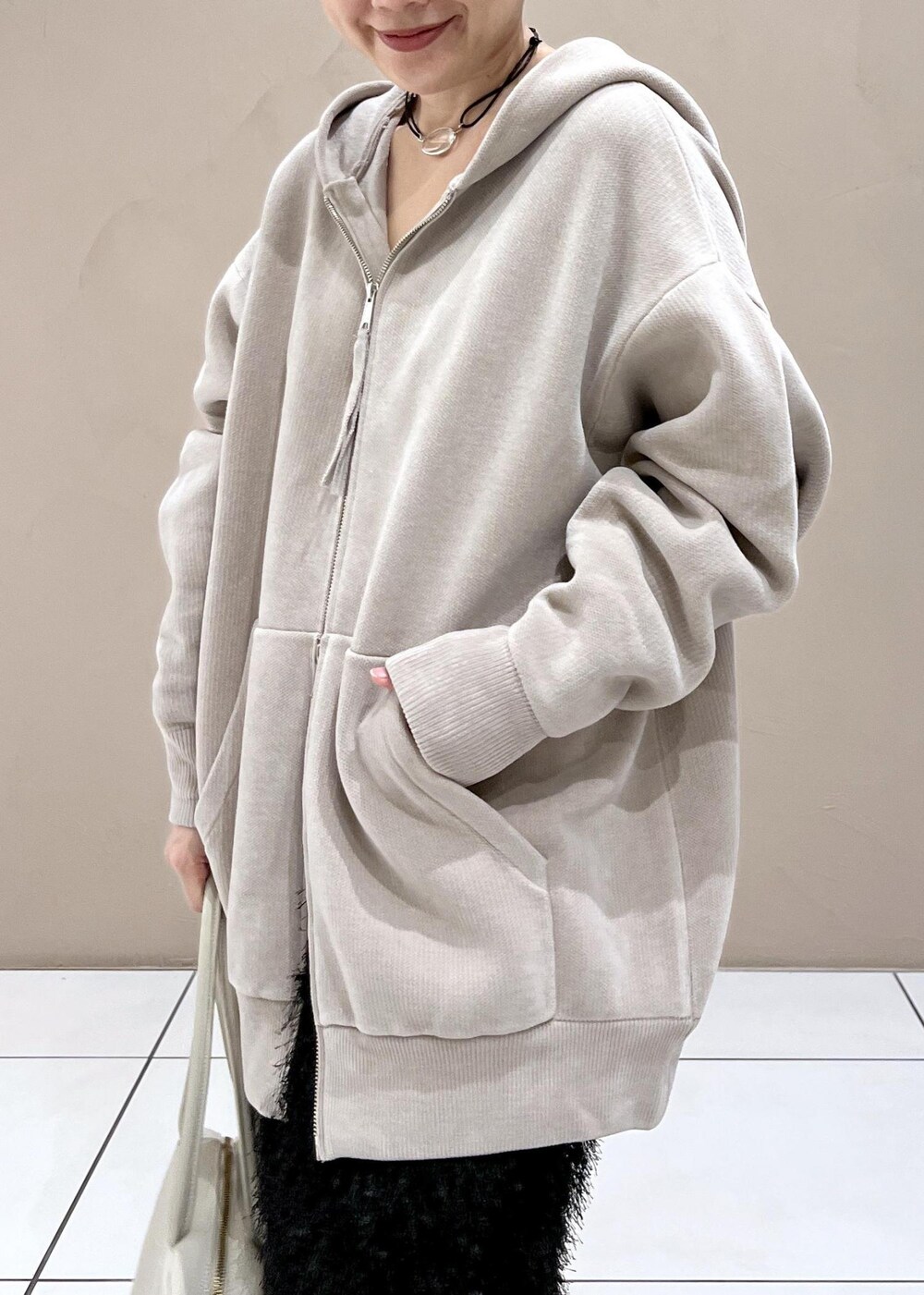 ベージュ系のパーカー、ホワイト系のボストンバッグ、ブラック系のブーツを着用したレディースの秋コーディネートの5枚目の写真