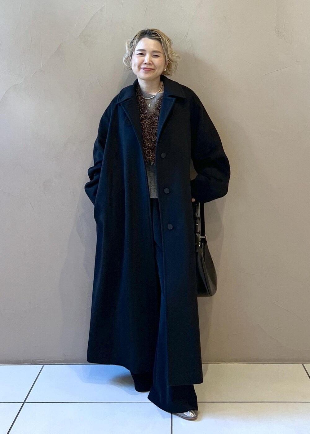 ブラック系のステンカラーコート、グレー系のニット/セーター、ブラック系のその他パンツを着用したレディースの冬コーディネートの9枚目の写真