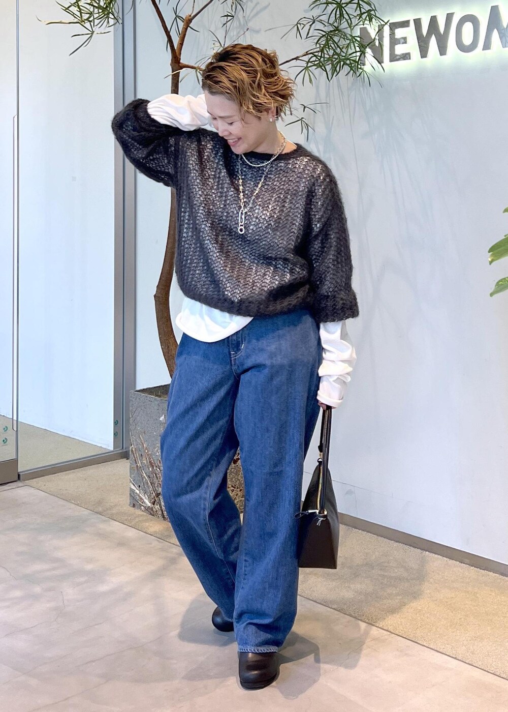 ブルー系のデニムパンツ、ブラック系のハンドバッグ、ブラック系のスニーカーを着用したレディースの秋コーディネートの3枚目の写真