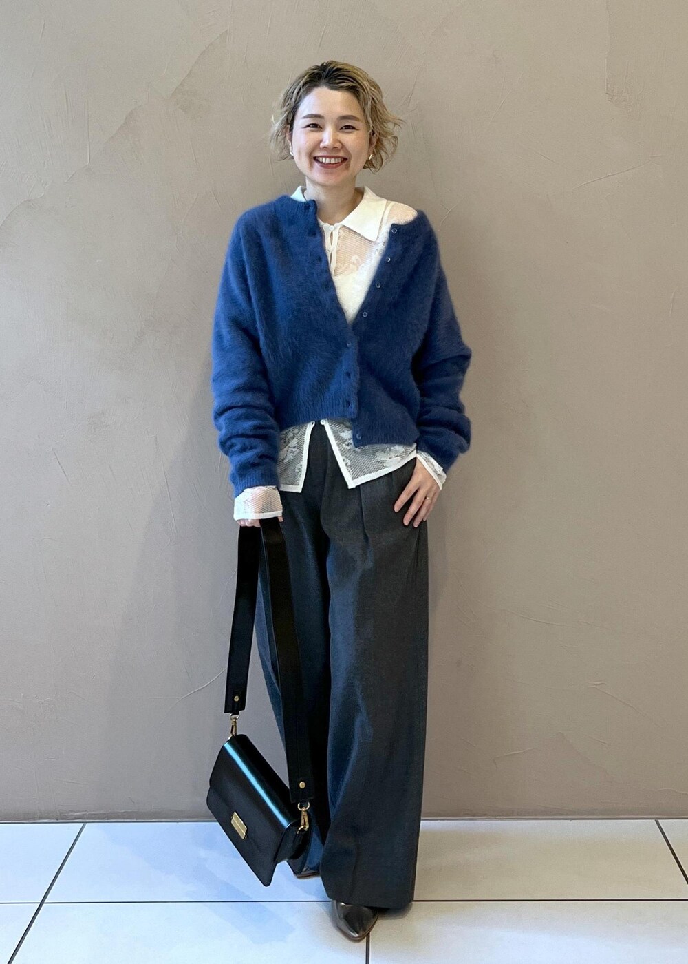 ブラック系のショルダーバッグ、ブルー系のカーディガン/ボレロ、グレー系のスラックスを着用したレディースの冬コーディネートの2枚目の写真