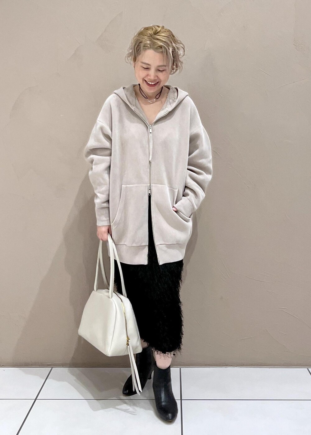 ベージュ系のパーカー、ホワイト系のボストンバッグ、ブラック系のブーツを着用したレディースの秋コーディネートの3枚目の写真