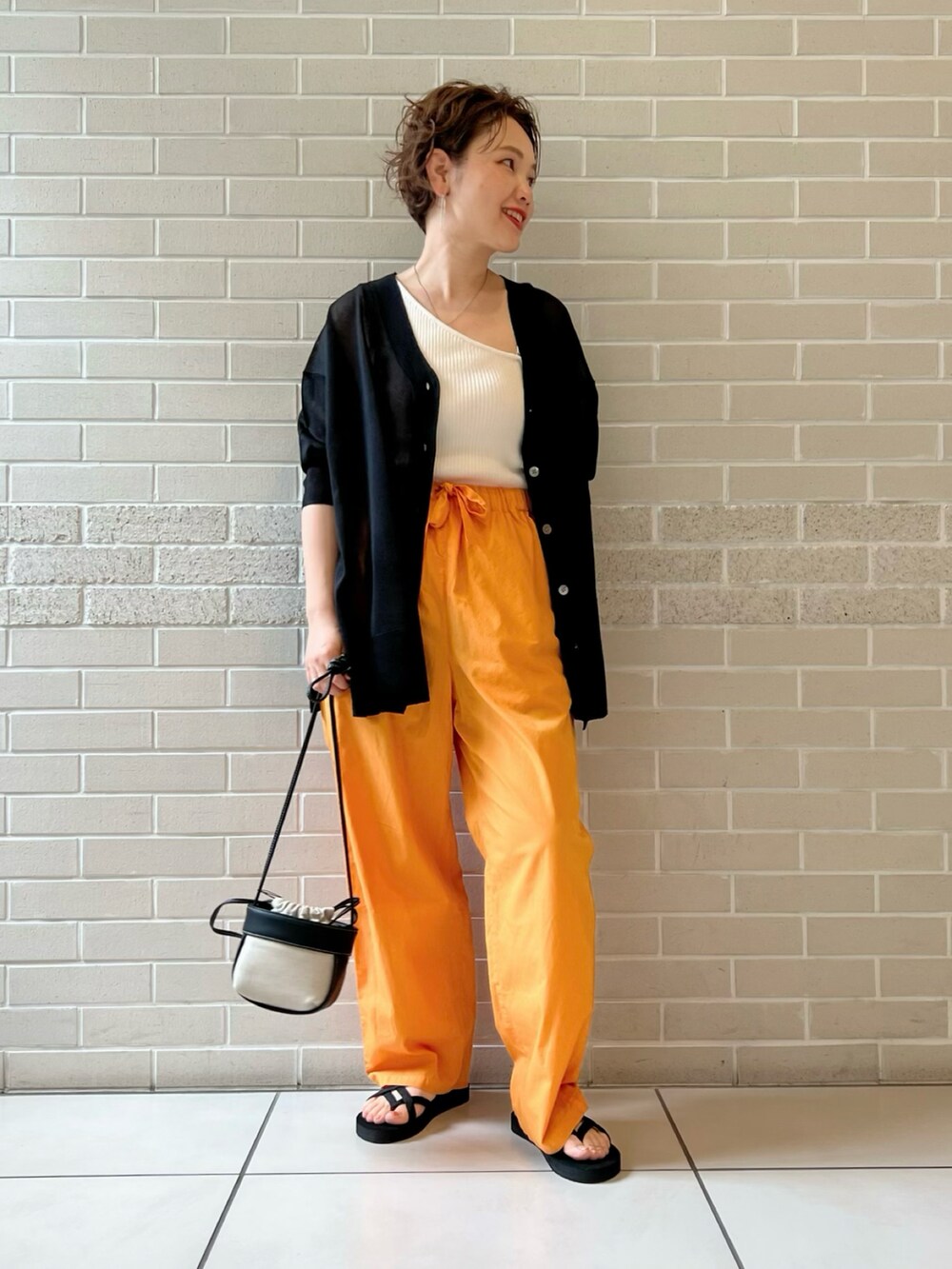 ブラック系のカーディガン/ボレロ、オレンジ系のパンツ、ブラック系のショルダーバッグを着用したレディースの夏コーディネートの2枚目の写真