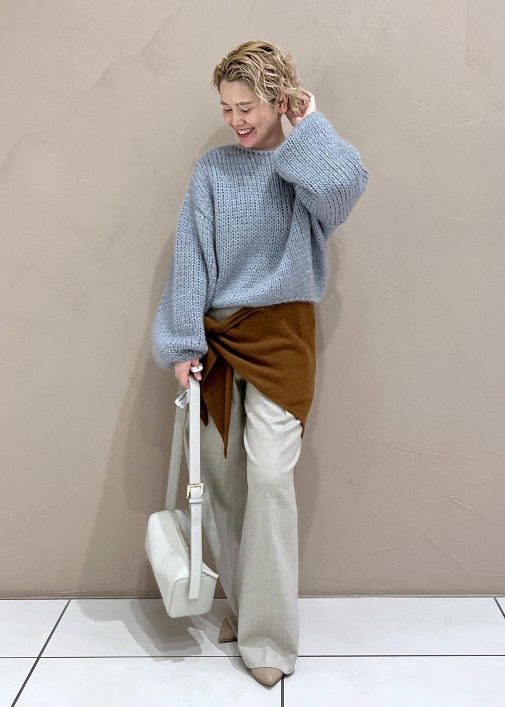 グレー系のショルダーバッグ、ベージュ系のスラックス、ブルー系のニット/セーターを着用したレディースの秋コーディネートの4枚目の写真