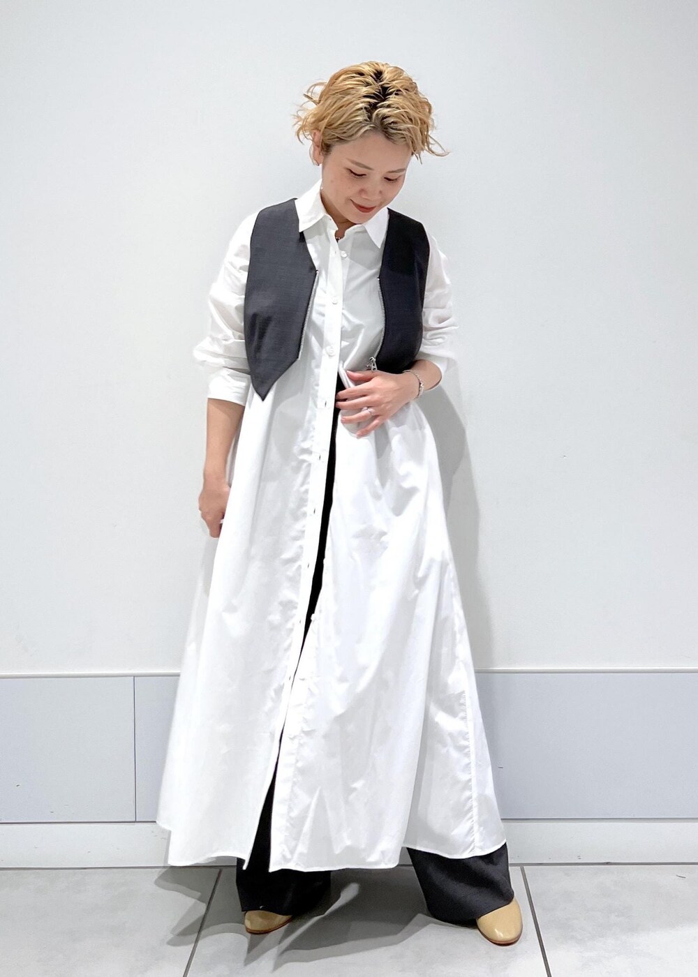 ホワイト系のシャツワンピース、ブラック系のタンクトップ、グレー系のベストを着用したレディースの秋コーディネートの2枚目の写真