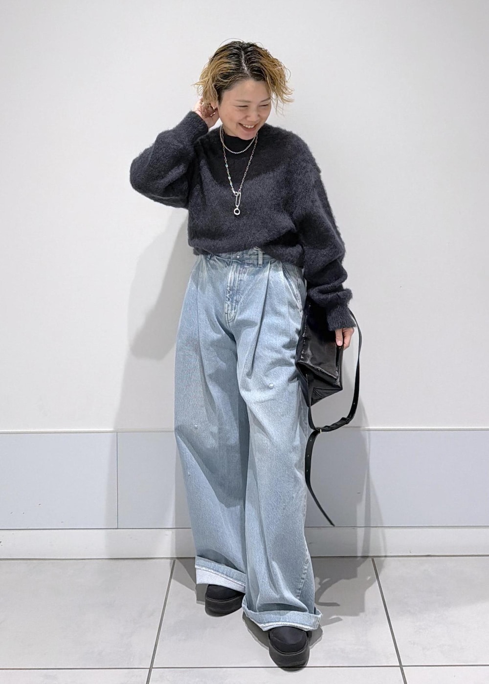 ブラック系のショルダーバッグ、ブラック系のブーツ、ブルー系のデニムパンツを着用したレディースの秋コーディネートの4枚目の写真