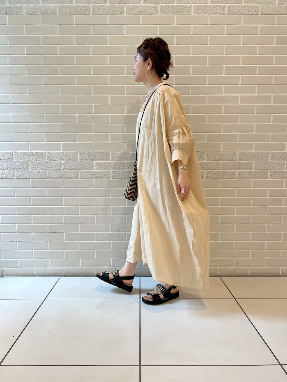 ブラウン系のショルダーバッグ、ブラック系のサンダル、ベージュ系のワンピースを着用したレディースの春コーディネートの3枚目の写真