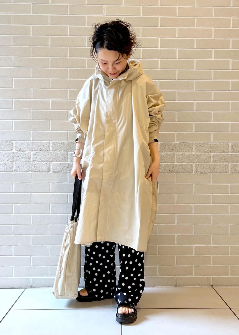 ベージュ系のトートバッグ、ブラック系のつなぎ/オールインワン、ベージュ系のレインコート/ポンチョを着用したレディースの夏コーディネートの4枚目の写真