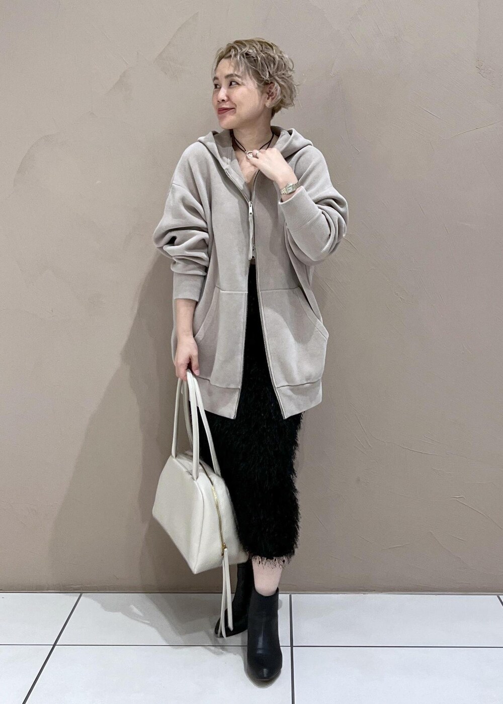 ベージュ系のパーカー、ホワイト系のボストンバッグ、ブラック系のブーツを着用したレディースの秋コーディネートの2枚目の写真