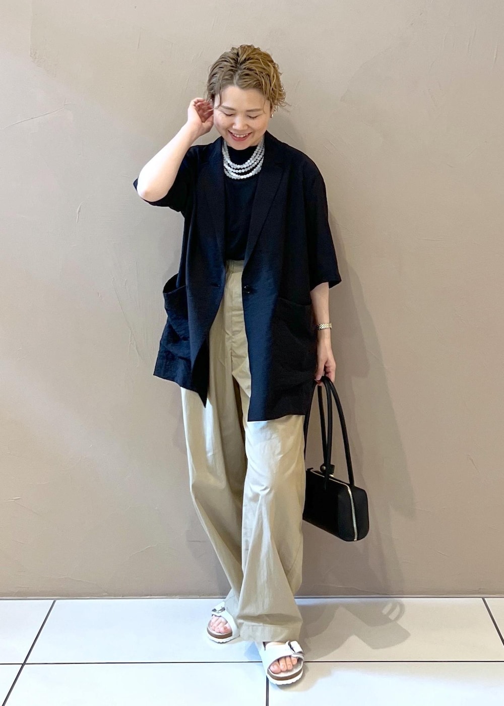 ベージュ系のその他パンツ、ブラック系のショルダーバッグ、ホワイト系のサンダルを着用したレディースの夏コーディネートの4枚目の写真