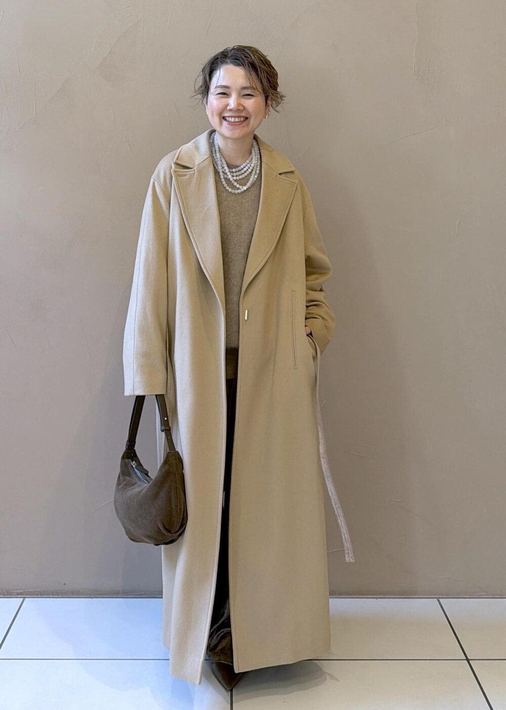 イエロー系のトレンチコート、ゴールド系のその他パンツ、ベージュ系のニット/セーターを着用したレディースの冬コーディネートの3枚目の写真