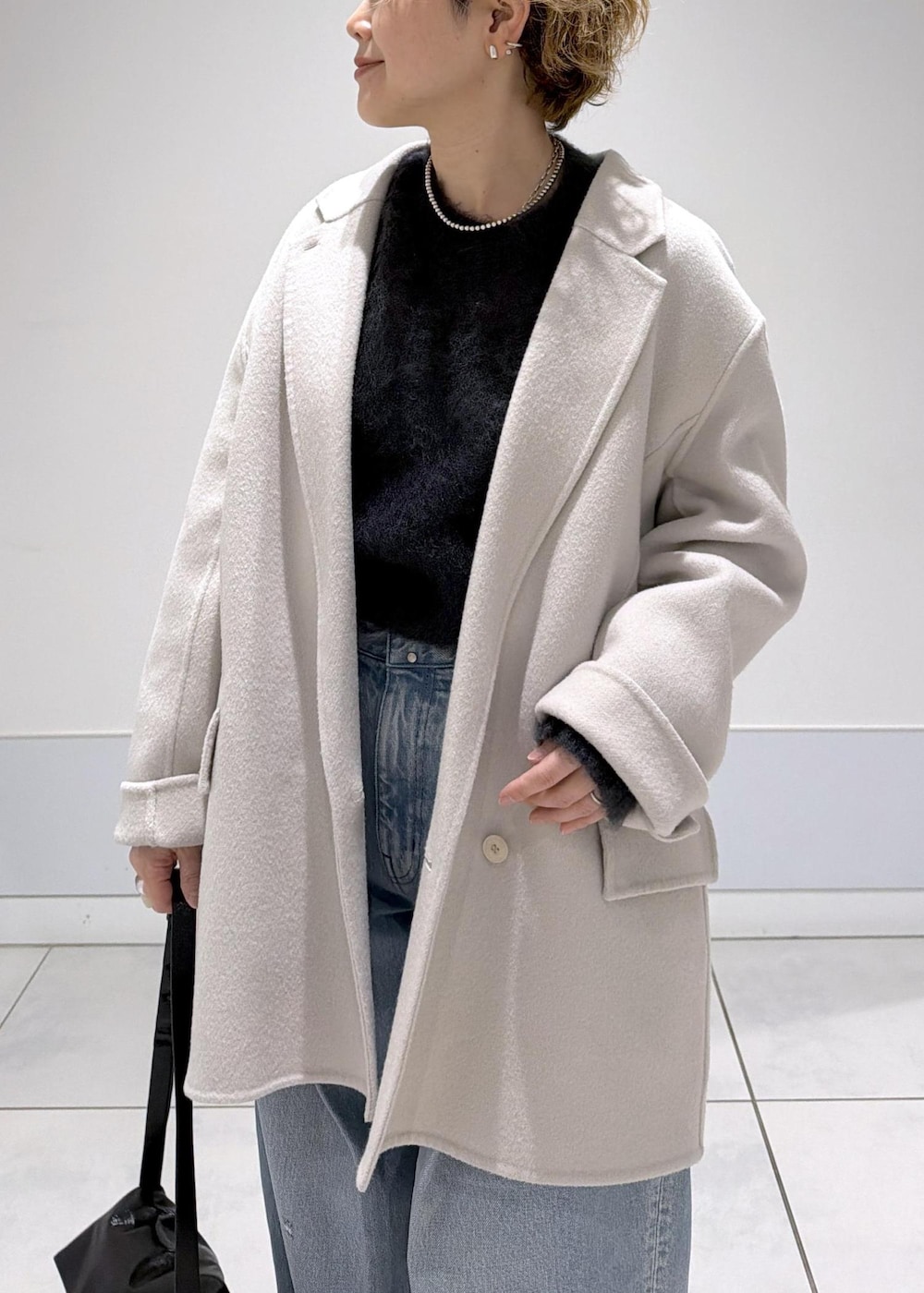 ブラック系のショルダーバッグ、ホワイト系のその他アウター、ブラック系のブーツを着用したレディースの秋コーディネートの6枚目の写真