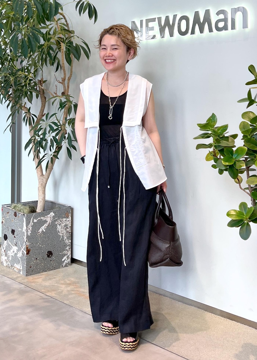 ブラック系のその他パンツ、ブラウン系のトートバッグ、ホワイト系のシャツ/ブラウスを着用したレディースの夏コーディネートの3枚目の写真