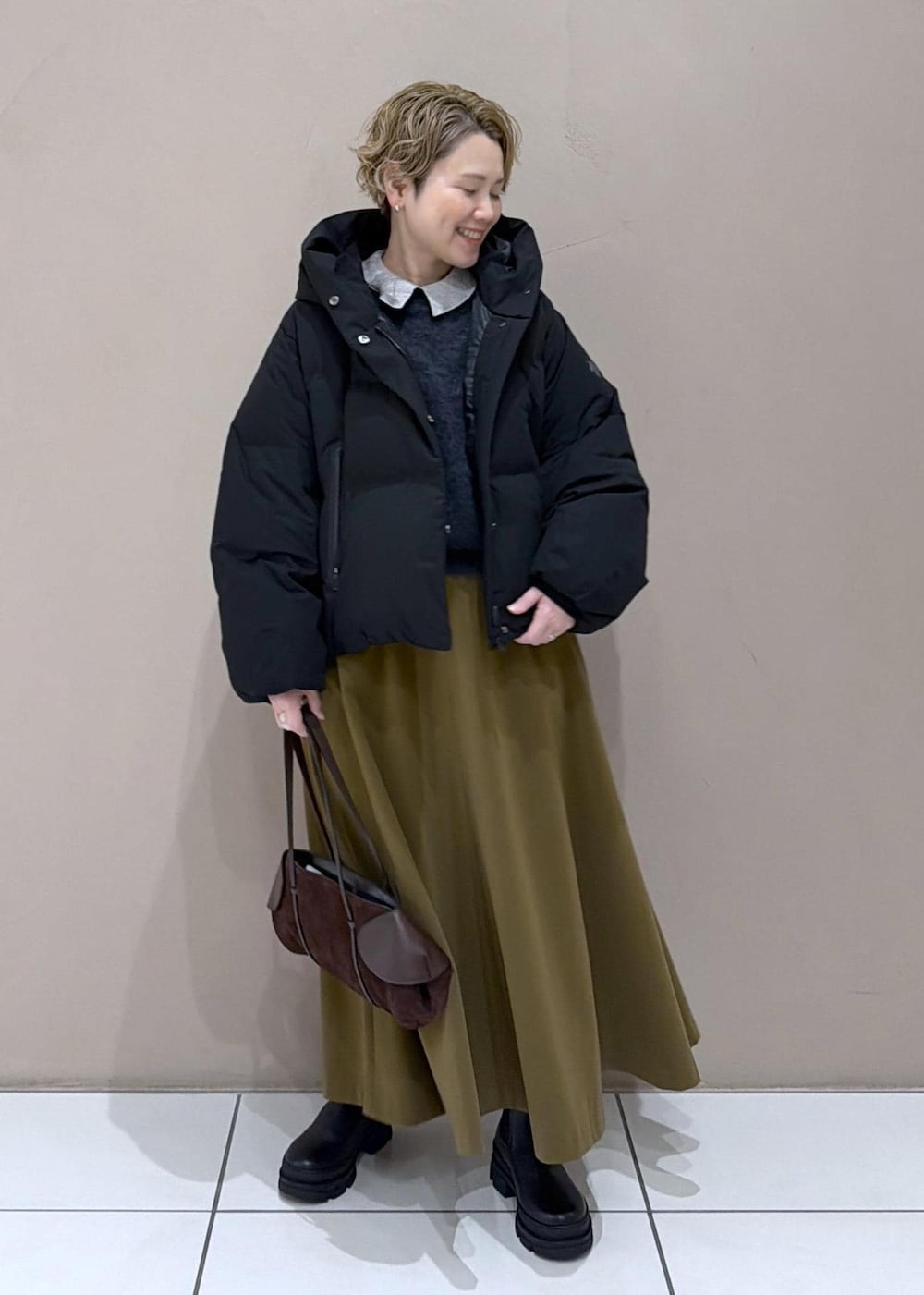 ブラウン系のスカート、ブラック系のダウンジャケット/コート、グレー系のニット/セーターを着用したレディースの冬コーディネートの3枚目の写真