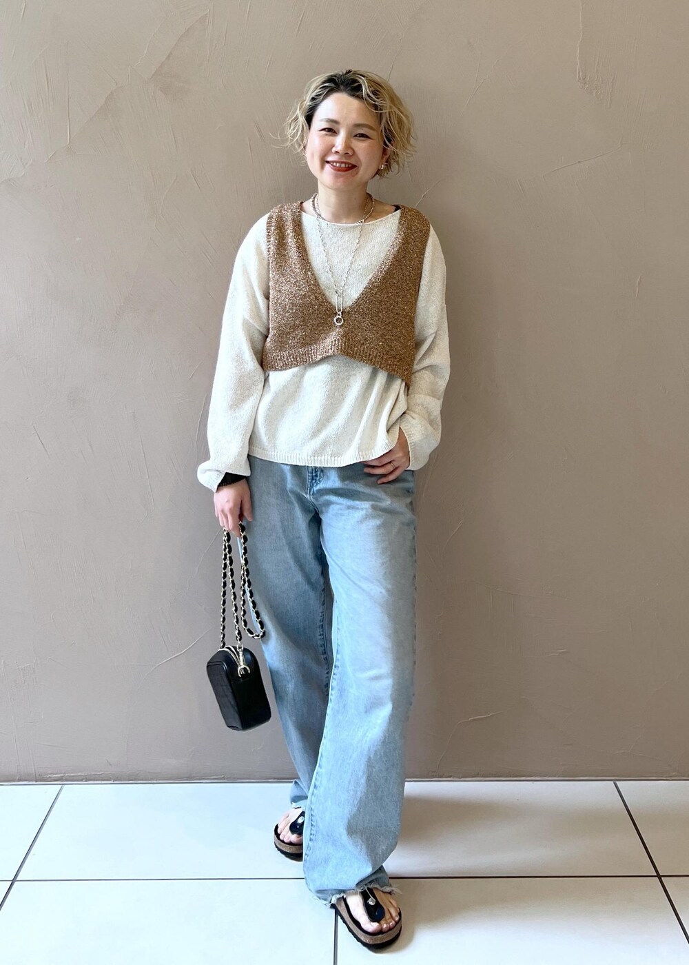 ブラック系のショルダーバッグ、ブルー系のデニムパンツ、ホワイト系のニット/セーターを着用したレディースの春コーディネートの2枚目の写真