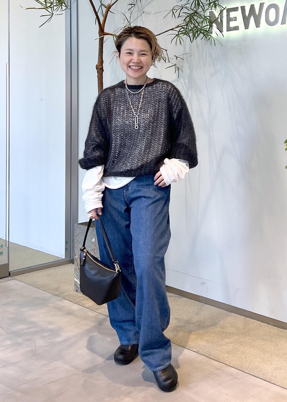 ブルー系のデニムパンツ、ブラック系のハンドバッグ、ブラック系のスニーカーを着用したレディースの秋コーディネートの4枚目の写真