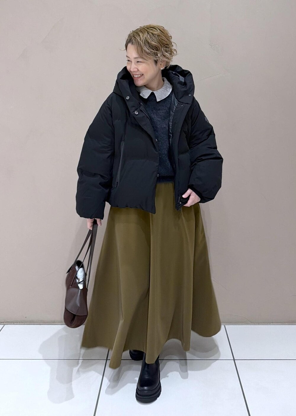 ブラウン系のスカート、ブラック系のダウンジャケット/コート、グレー系のニット/セーターを着用したレディースの冬コーディネートの2枚目の写真