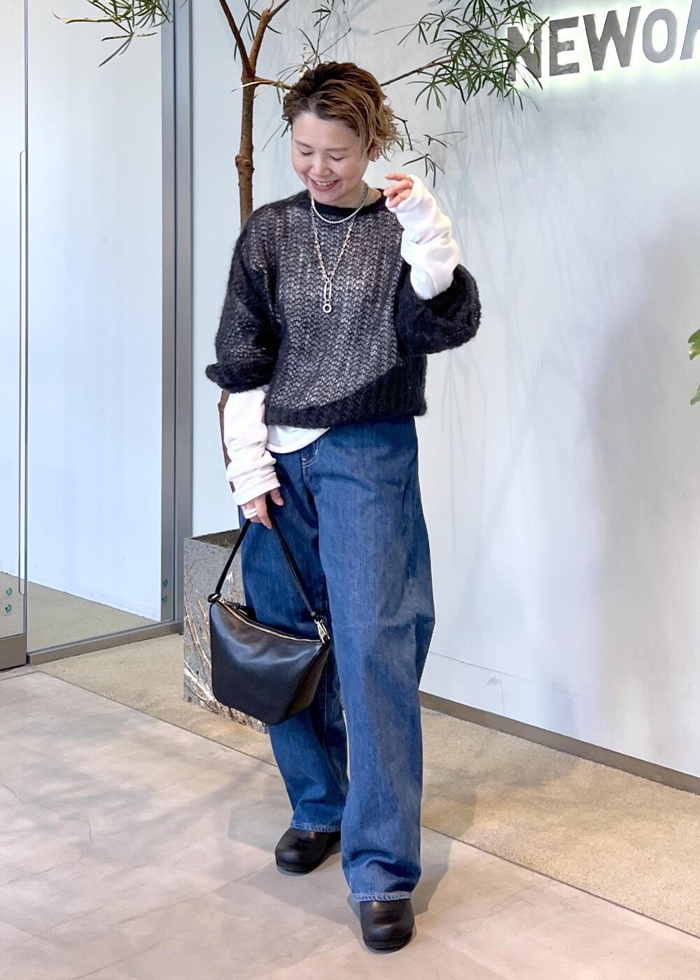 ブルー系のデニムパンツ、ブラック系のハンドバッグ、ブラック系のスニーカーを着用したレディースの秋コーディネートの2枚目の写真