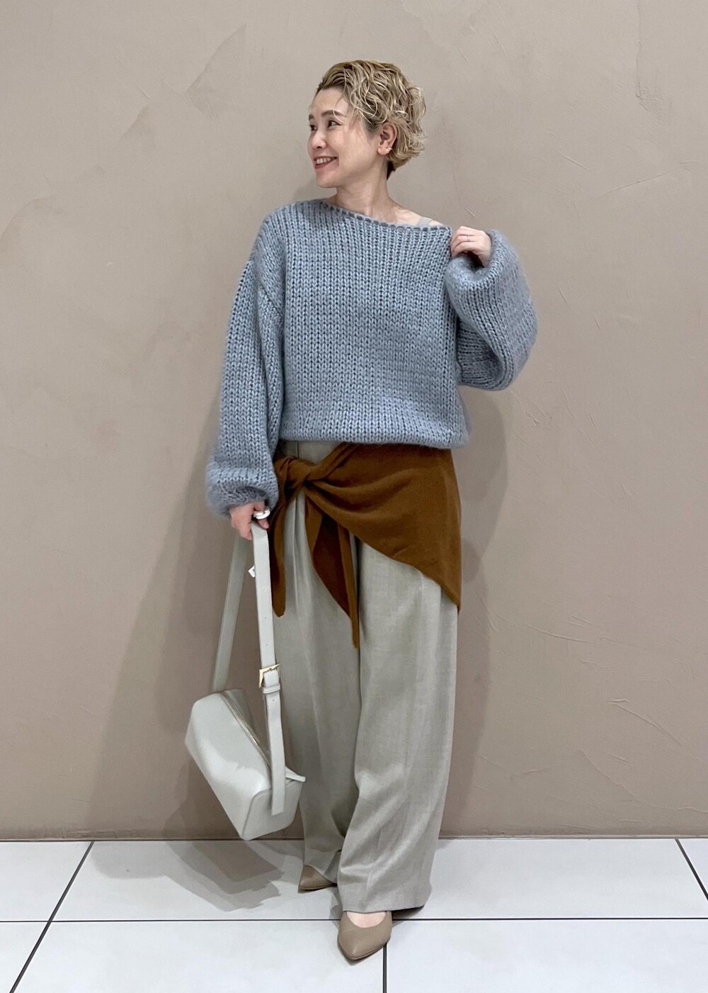 グレー系のショルダーバッグ、ベージュ系のスラックス、ブルー系のニット/セーターを着用したレディースの秋コーディネートの2枚目の写真