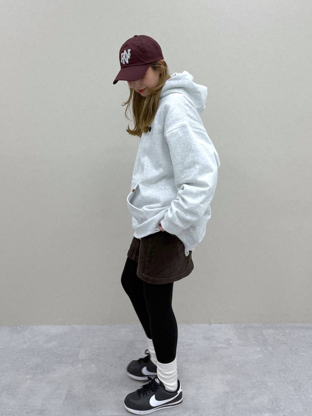 ブラウン系のスカート、グレー系のパーカー、レッド系のキャップを着用したレディースの秋コーディネートの2枚目の写真