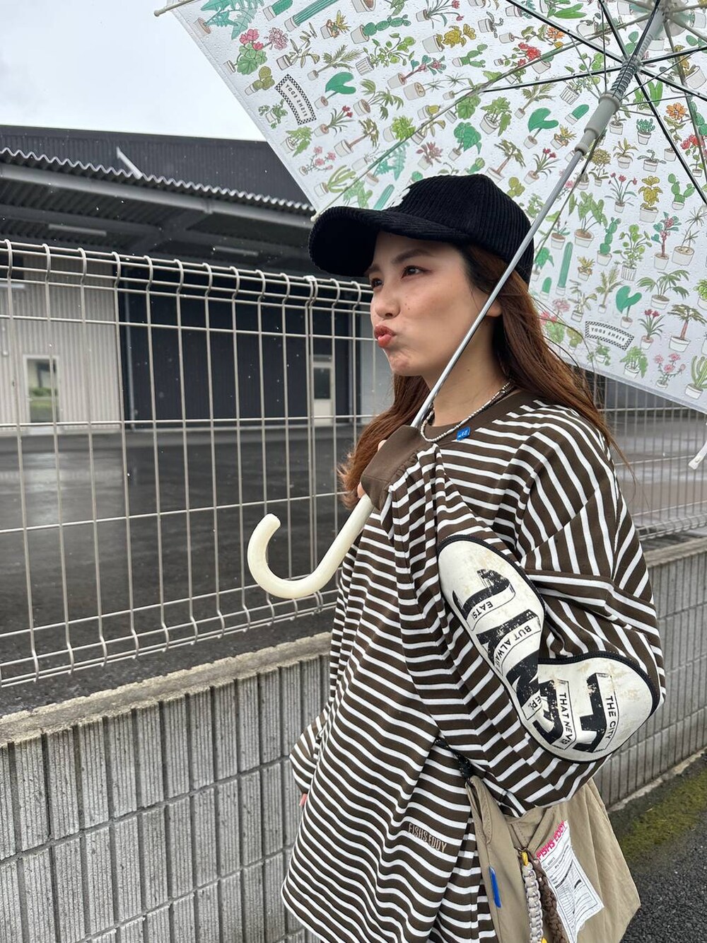 ベージュ系のショルダーバッグ、その他の長傘、ブラック系のキャップを着用したレディースの秋コーディネートの2枚目の写真