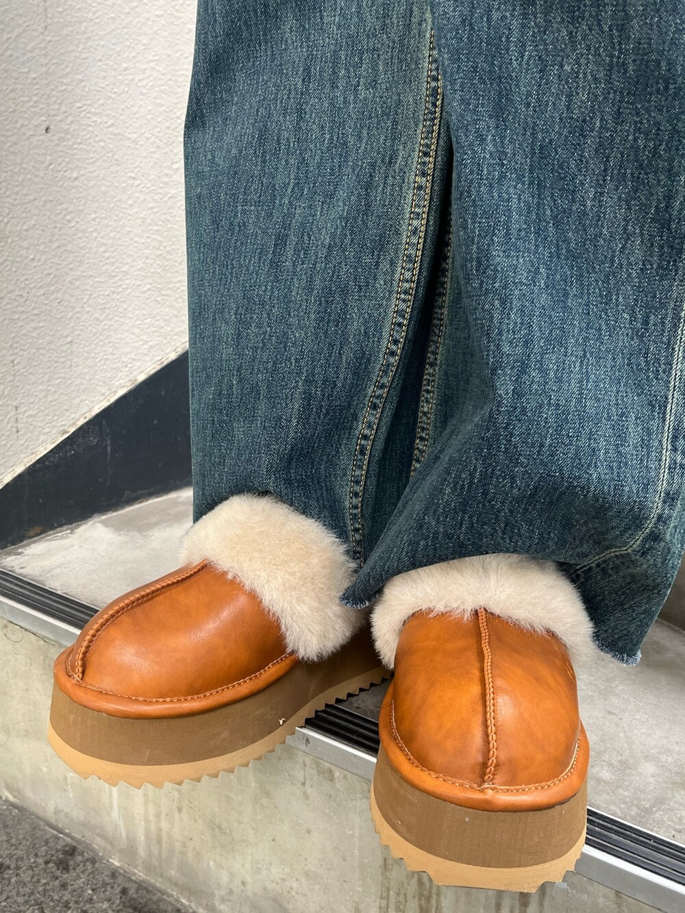 ブラウン系のムートンコート、ホワイト系のニット/セーター、ブルー系のデニムパンツを着用したレディースの冬コーディネートの6枚目の写真