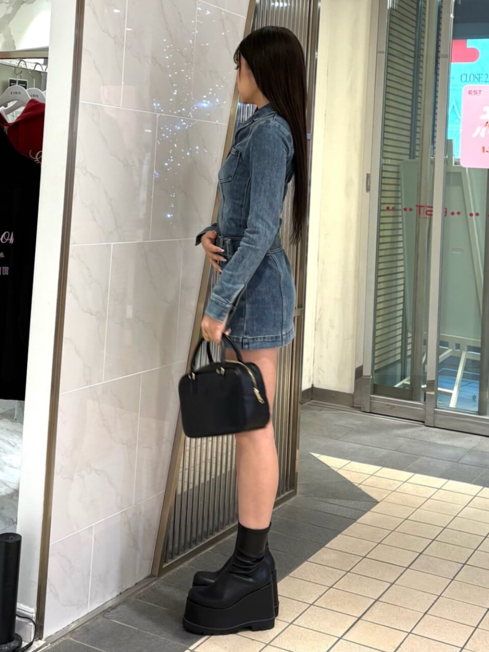 ブラック系のハンドバッグ、ブルー系のワンピース、ブラック系のブーツを着用したレディースの冬コーディネートの2枚目の写真