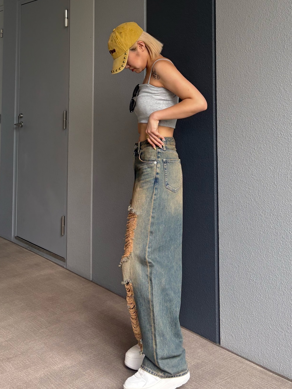 グレー系のワンピース、ブルー系のデニムパンツ、イエロー系のキャップを着用したレディースの夏コーディネートの2枚目の写真