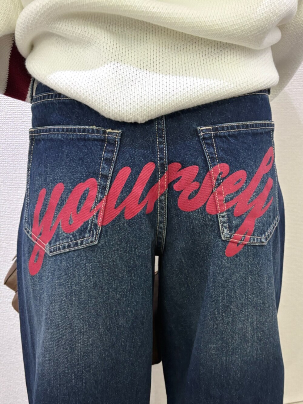 ブルー系のデニムパンツ、ブラウン系のハンドバッグ、ホワイト系のニット/セーターを着用したレディースの冬コーディネートの6枚目の写真